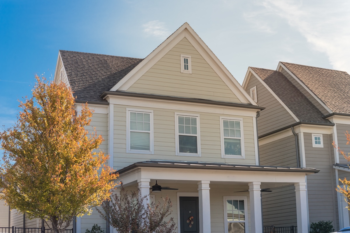 Upscale cottage style homes in suburbs Dallas, Texas with wood siding, covered porch patio with ceiling fans. Colorful autumn leaves and white cladding layer thermal insulation, weather resistance