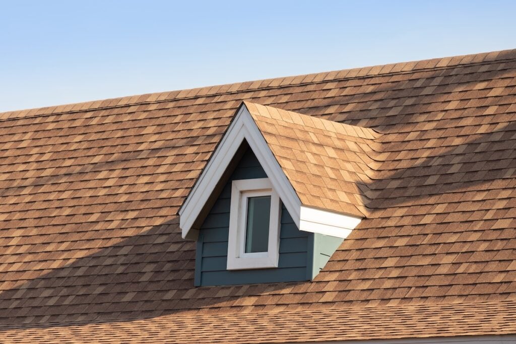 Roof shingles with garret house on top of the house. dark brown asphalt tiles on the roof background with blue sky.