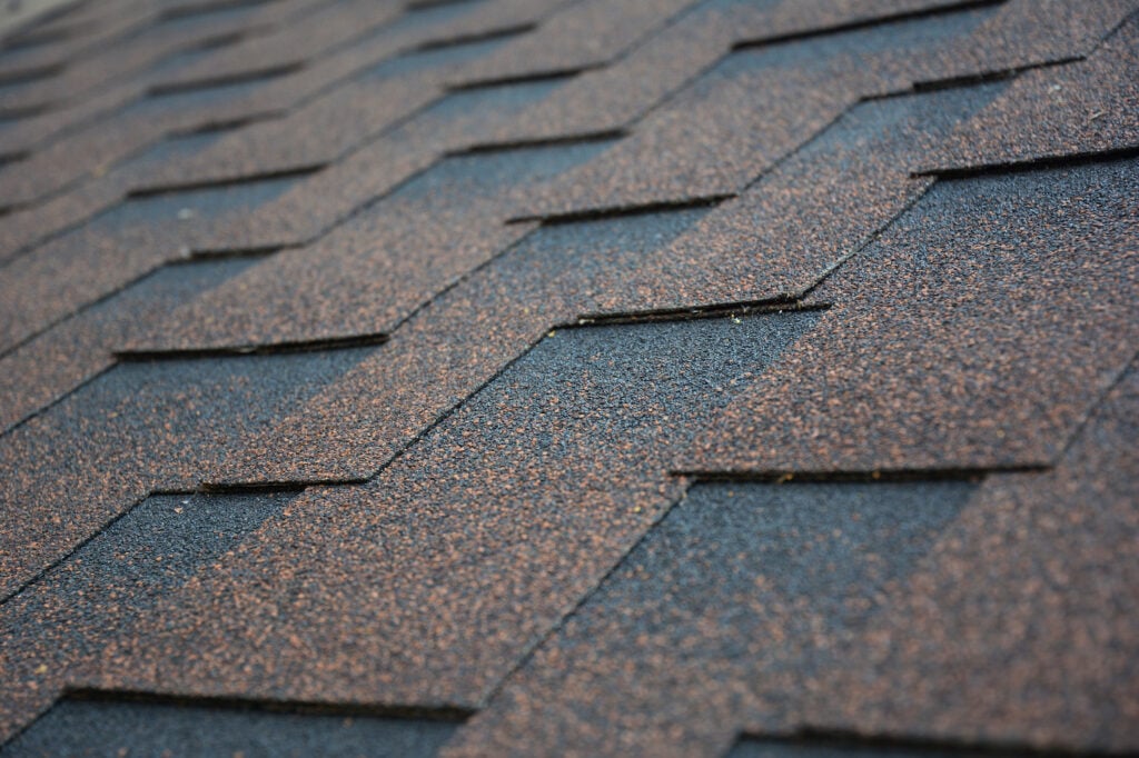 architectural shingles vs 3 tab Copper, brown architectural, dimensional asphalt roofing shingles background. A close-up of a roof covered with brown asphalt shingles.