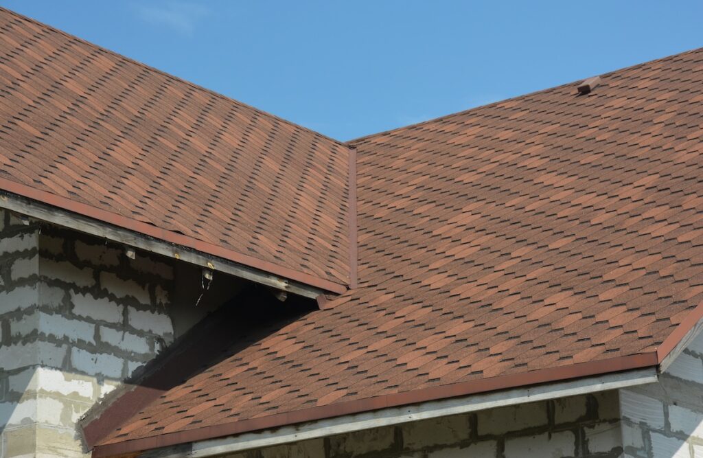roof flashing repair Brown asphalt shingled roof valley leaking problem area with a ventilation cap. A close-up of asphalt shingles installed on a roof valley with a waterproof flashing. Asphalt shingles roofing.