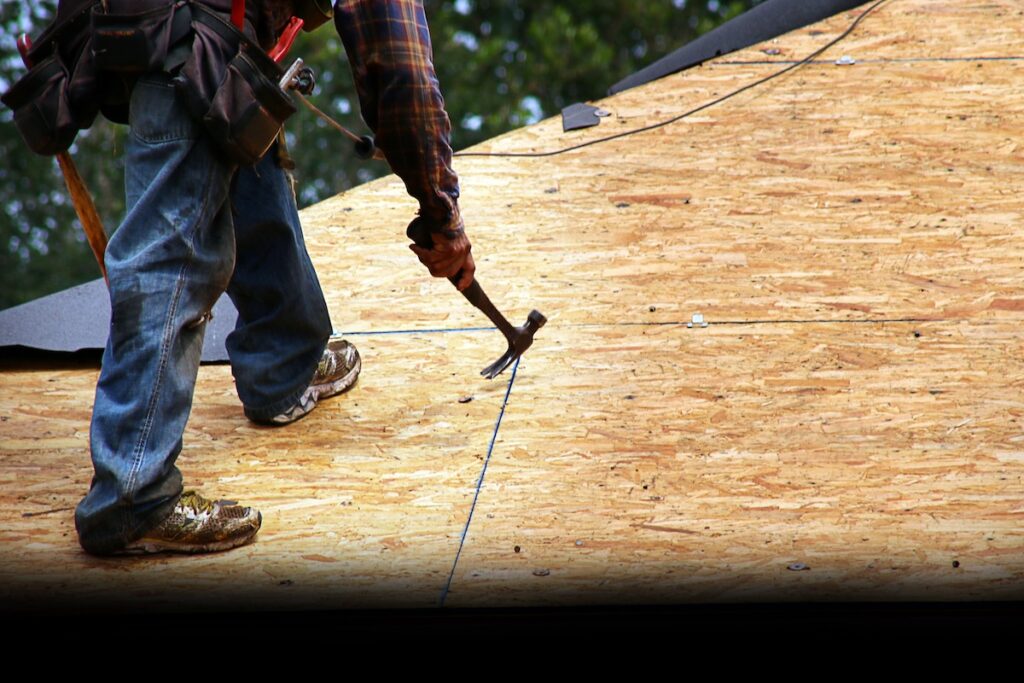 Worker using Nail Puller to remove excess nails on bare rooftop prior to new felt installation.
