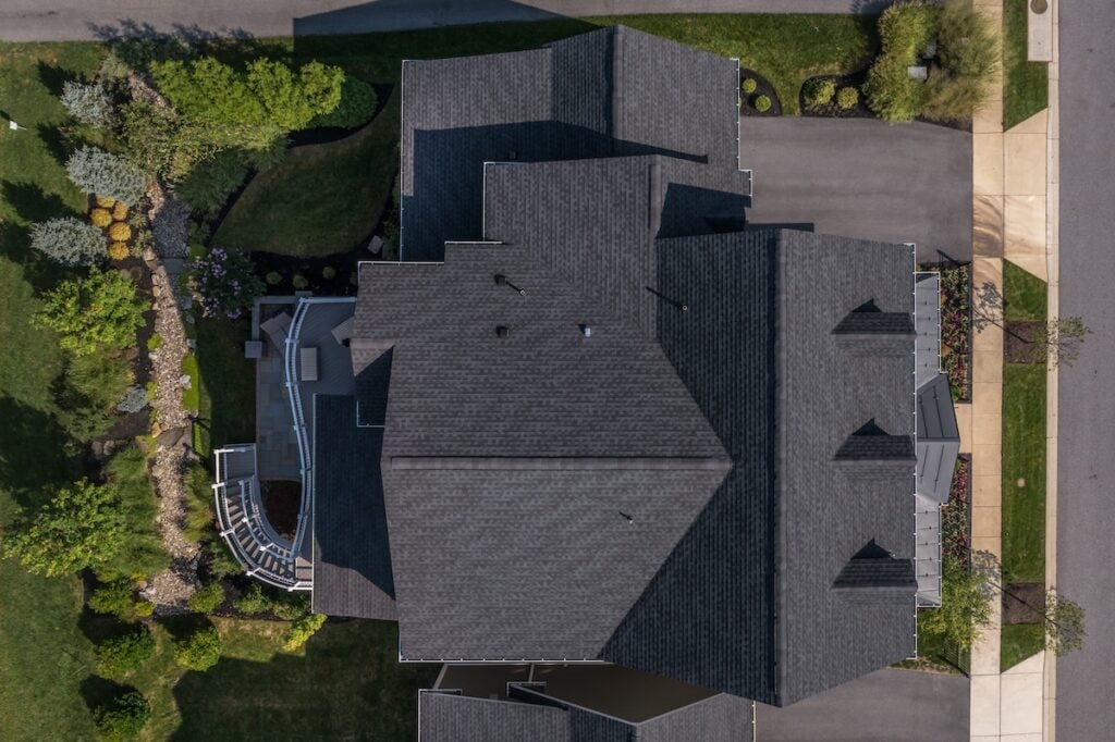 Aerial top down view of a complex hip and valley pitched roof with three dormers on a new construction American luxury single family house real estate