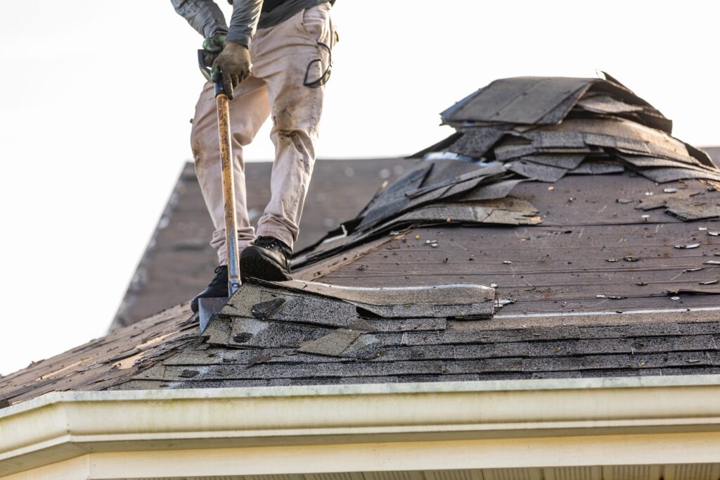 roofer working on residential house removing old roofing material with roof shingle remover shovel.