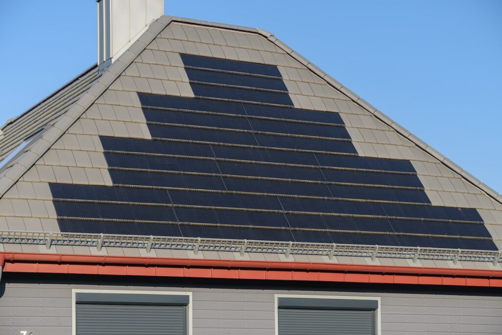 High-tech solar roof tiles on roof as solar power plant. Solar shingles installed on roof of residential home. Solar roof tiles integrated into roof. Building-integrated photovoltaic systems.