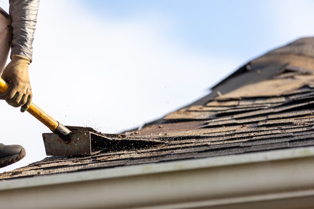 roofer working on residential house removing old roofing material with roof shingle remover shovel.