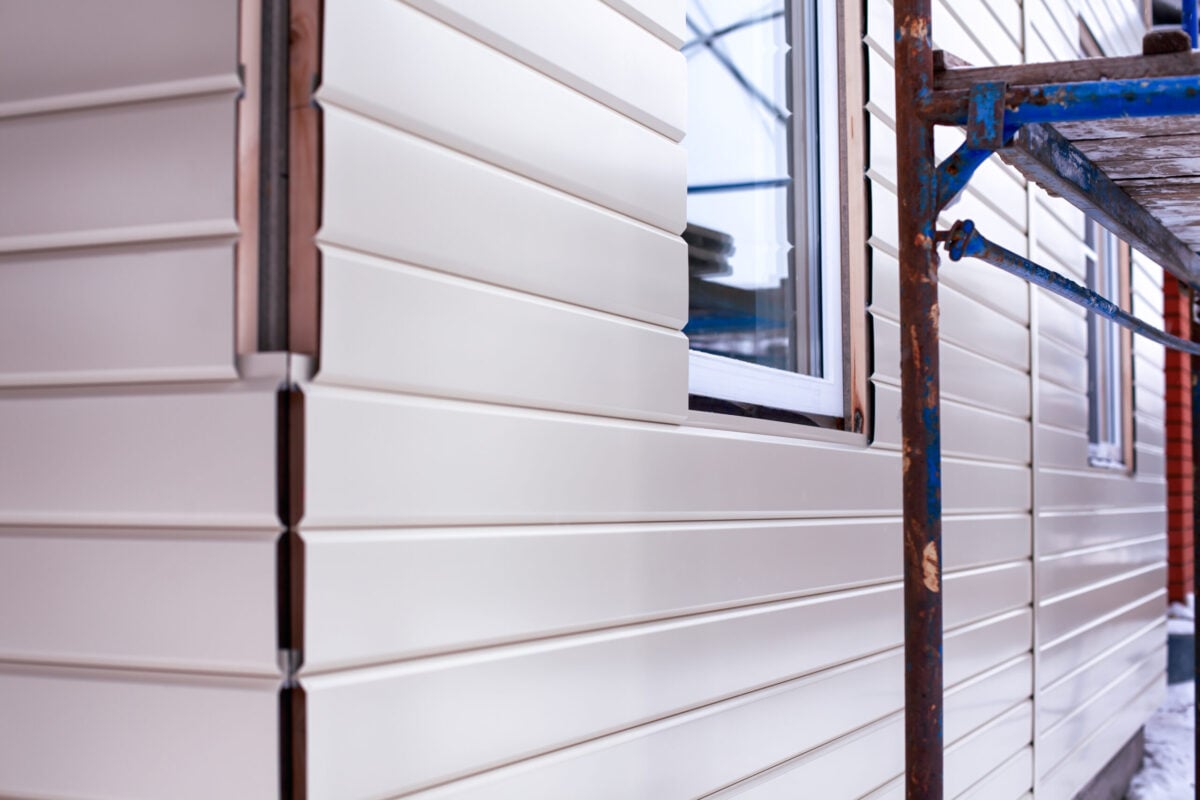 House corner with beige siding covering the walls and scaffolding. Closeup.