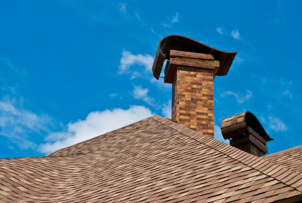 curling shingles The roof of the house with two chimneys in the new design against the blue sky with clouds.