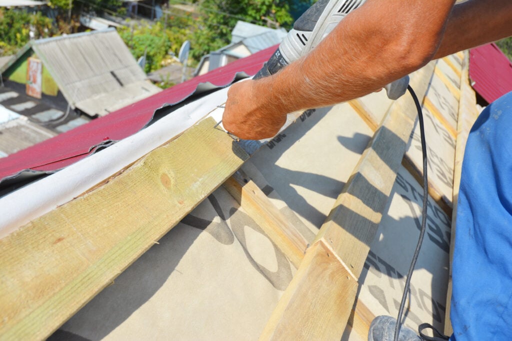 Roofer during metal roofing construction: A close-up on unfinished roof ridge with a vapor, moisture barrier and lightweight metal roofing sheets installed over a roofing deck, sheathing.